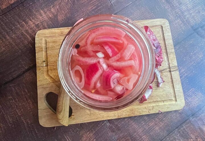 Pickled red onions and peppercorn in glass jar.