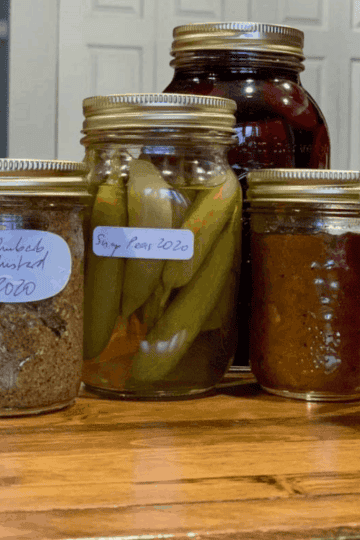 5 mason jars with pickled vegetables and preserves on a wooden counter