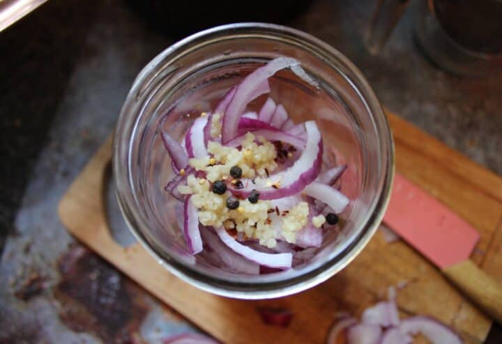 Red onion slices, peppercorns and garlic in glass mason jar