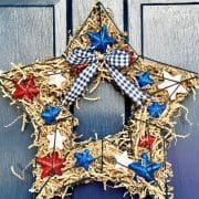 A rustic DIY patriotic wreath swith red, white, and blue accents, adorned with a black and white gingham ribbon, hanging on a blue door.
