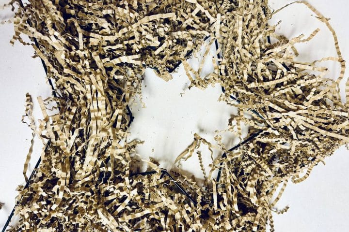 A DIY patriotic wreath made from shredded brown paper is arranged in a star-like shape on a white surface.