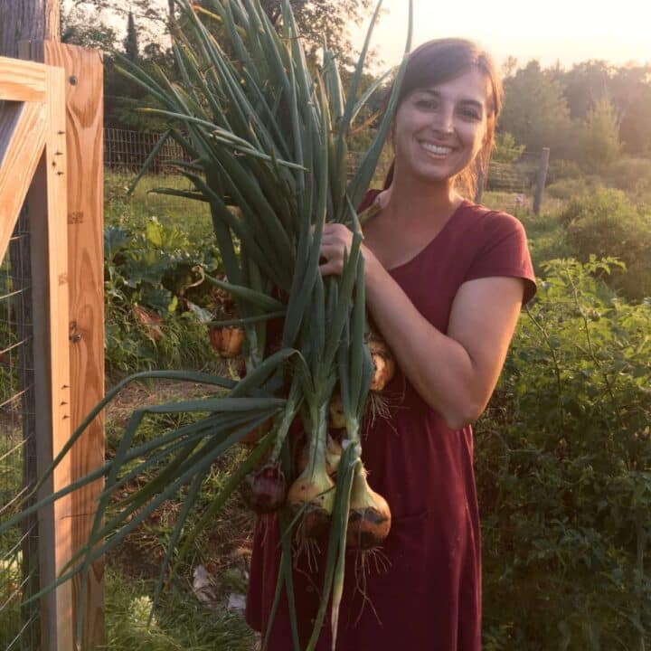 Sadie of the Wisconsin Homesteader holding a bunch of onions.