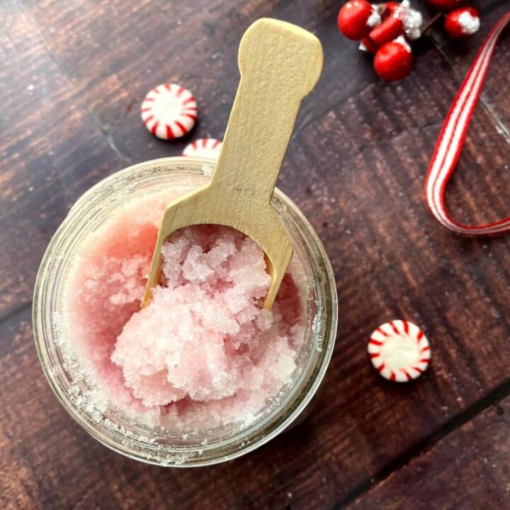 A jar of pink peppermint sugar with a spoon and candy canes.