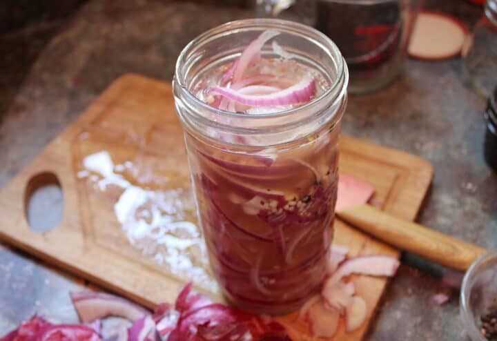 Side view of pickled red onions in glass jar on wooden cutting board