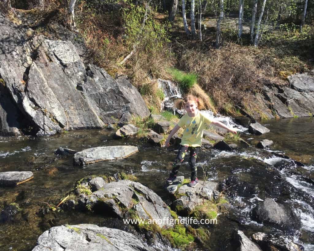 Young girl standing on a rock in a stream outdoors in the summer