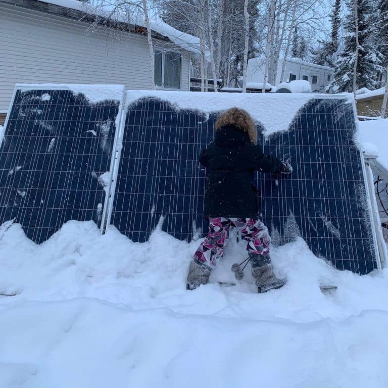 A little girl standing next to a snow-covered solar panel, showcasing the potential to survive off the grid with renewable energy.