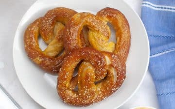 Three sourdough pretzels served on a white plate next to a blue napkin.
