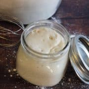 A jar of sourdough discard and a whisk on a table.