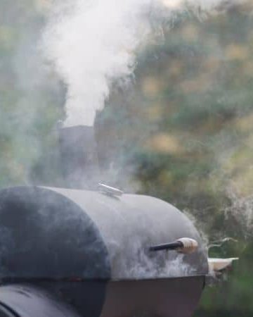 A black charcoal smoker with smoke coming out of the top dampener