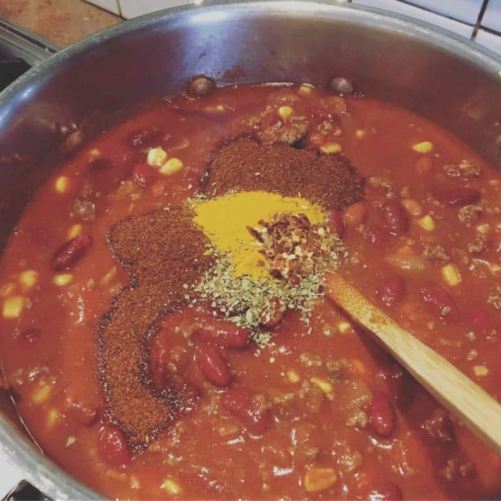 A pot of chili with spices and a wooden spoon.