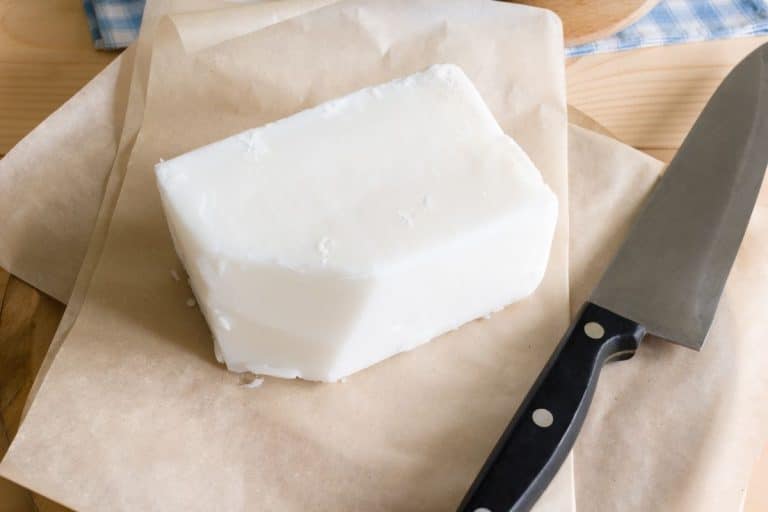 A block of tallow rests on parchment paper beside a black-handled knife, reminiscent of traditional uses for tallow in cooking and crafts.