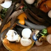 A bag filled with food waste for composting: banana peels, eggshells, orange peels, a paper tag, and other organic material.