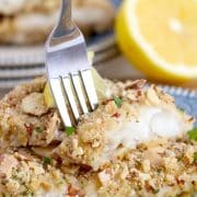 A fork is holding a piece of breaded walleye with lemon on a plate.