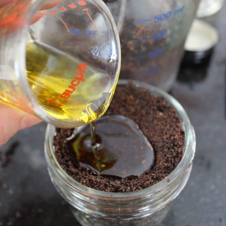 A person pouring oil into a jar of coffee grounds for coffee brown sugar scrub.