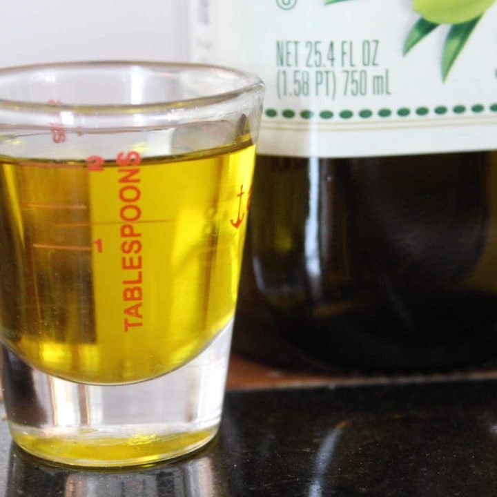 A shot glass of olive oil next to a bottle of olive oil.
