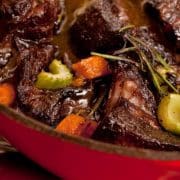 Stewed beef with vegetables in a red pan.