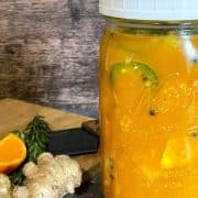 A jar of orange and ginger juice on a cutting board.
