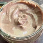 Top view of a glass jar filled with creamy chocolate mousse, showing a smooth, swirled texture on a wooden table.