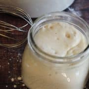 A jar of flour and a whisk on a table.