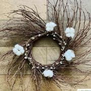 A rustic twig wreath adorned with cotton bolls against a wooden background.