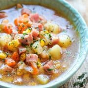 A bowl of soup with ham, potatoes and carrots.
