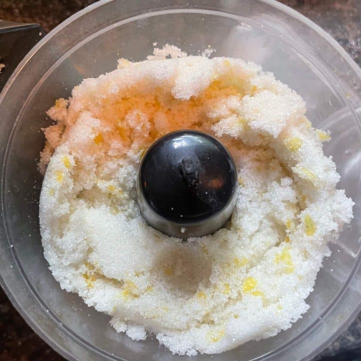 A food processor filled with sugar and chunks of lemon.