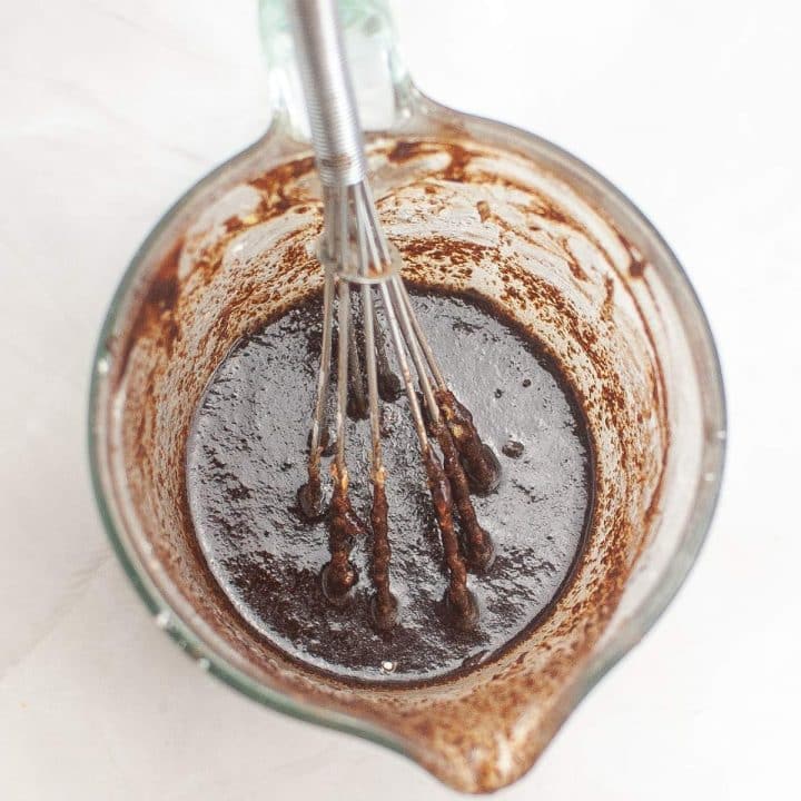 A whisk in a glass bowl with chocolate batter.