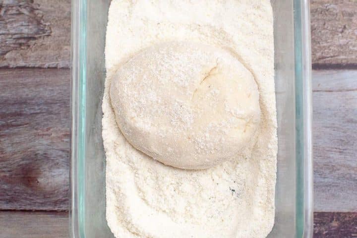 A ball of dough coated in flour inside a glass baking dish, placed on a wooden surface.