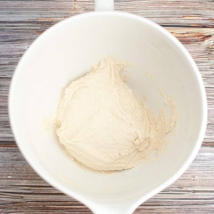 A top-down view of a white cup containing a small amount of dough on a wooden surface.