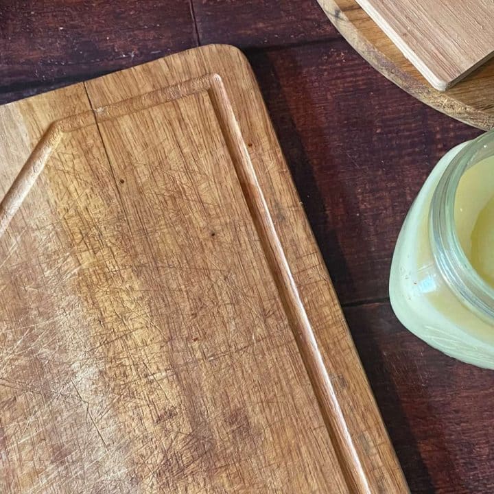 A wooden cutting board with a jar of DIY wood butter on it.